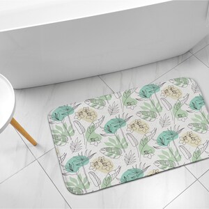 May include: A white bath mat with a green and yellow tropical leaf pattern. The mat is made of a soft, absorbent material and is perfect for adding a touch of style to your bathroom.