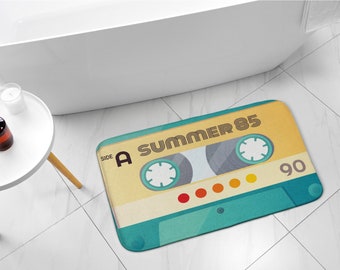 Könnte beinhalten: Eine türkisfarbene und gelbe Badematte mit einem Retro-Kassettenband-Design. Das Band trägt die Aufschrift "Side A Summer 85" und "90".