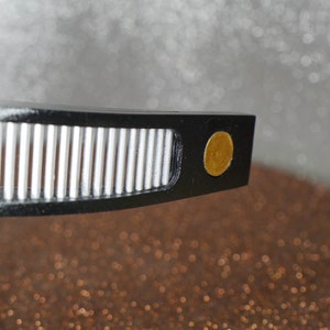 May include: Close-up of a black record player tonearm with a gold-colored counterweight.
