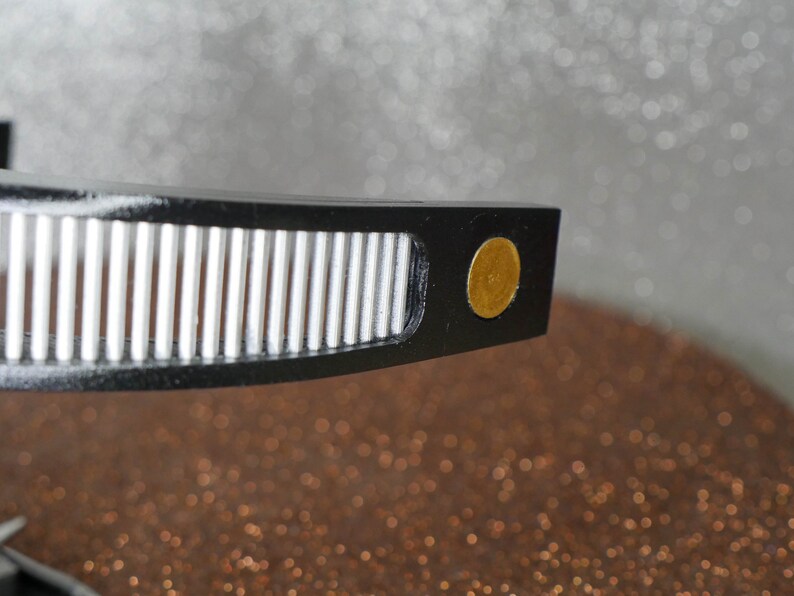 May include: Close-up of a black record player tonearm with a gold-colored counterweight.