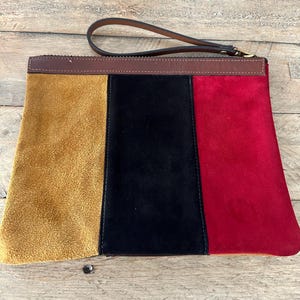 Puede incluir: Un bolso de mano de ante tricolor con una correa de cuero marrón. El bolso está dividido en tres secciones: amarillo mostaza, negro y rojo.