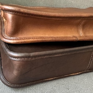 May include: Two rectangular leather bags stacked on top of each other. The top bag is a medium tan color with visible stitching along the edges. The bottom bag is a dark chocolate brown color with matching dark brown piping and stitched seams.