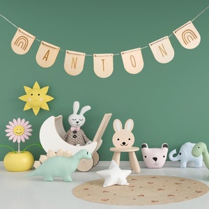May include: A green wall with a wooden banner that reads "ANTON", a stuffed bunny, a toy stroller, a wooden chair, a star-shaped pillow, and a variety of stuffed animals.