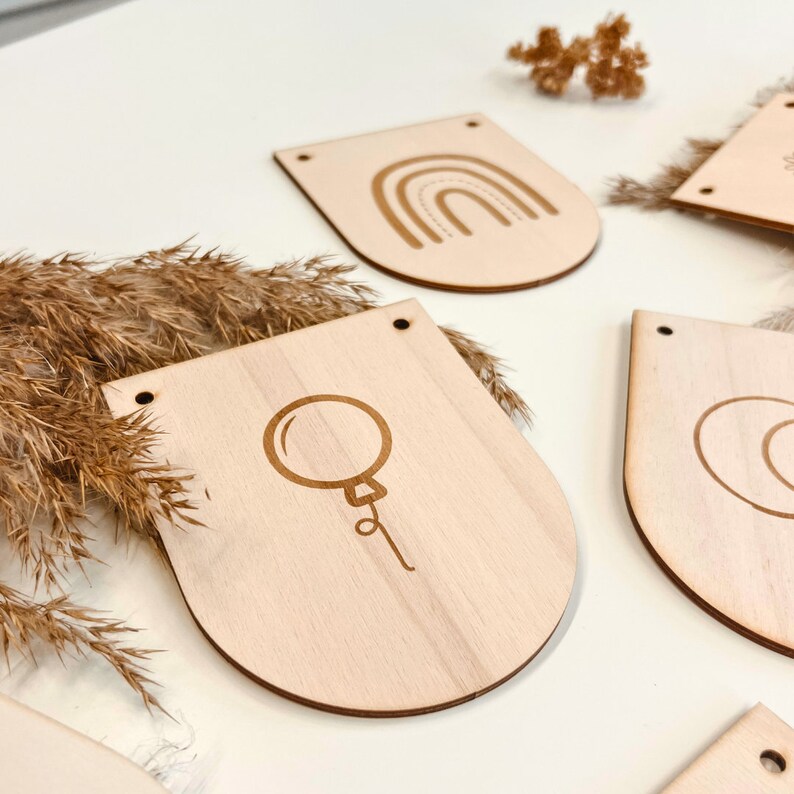 May include: Wooden banner flags with various designs, including a rainbow, a balloon, and a circle. The flags are unfinished and have a natural wood color.