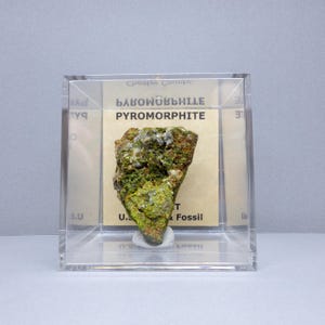 May include: A green and white pyromorphite mineral specimen in a clear acrylic display case. The label reads "Pyromorphite" and "БЛЫКОВАЯНЫЕ".