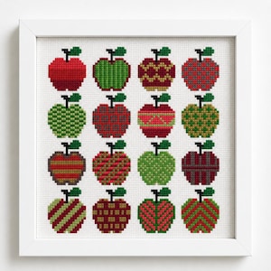 Op de afbeelding: Een ingelijst kruissteek kunstwerk met een raster van zestien appels in verschillende patronen en kleuren, waaronder rood, groen en kastanjebruin. Elke appel is weergegeven in een pixelstijl met een klein groen steeltje en blaadje.