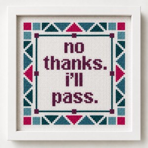 May include: Cross-stitch art in a white frame. The artwork features the phrase "no thanks. I'll pass." in purple letters on a white background. The border is decorated with teal, magenta, and dark green geometric shapes.