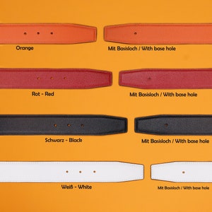 May include: Four leather belt straps in orange, red, black, and white. Each strap has multiple holes and is labeled with its color in German and English. The straps are all the same size and shape, and they are all lying flat on a yellow surface.