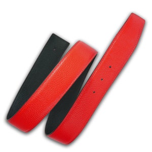 Può includere: Una cintura in pelle reversibile con un lato rosso e un lato nero. La cintura è realizzata in pelle testurizzata e ha un design classico.