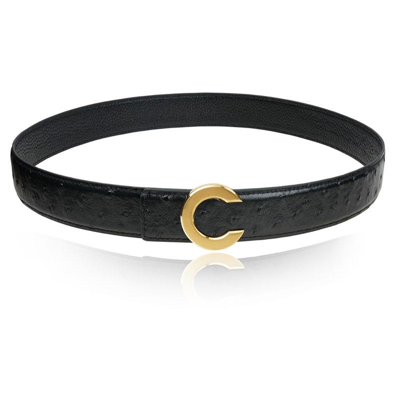 Puede incluir: Un cintur&oacute;n de cuero negro con un patr&oacute;n de piel de avestruz y una hebilla dorada en forma de C.