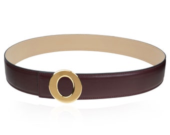 Puede incluir: Un cinturón de cuero burdeos con una hebilla circular dorada. El cinturón tiene un interior beige claro. La hebilla es una característica destacada, que añade un toque de elegancia al accesorio. Diseñado para tallas de cintura.