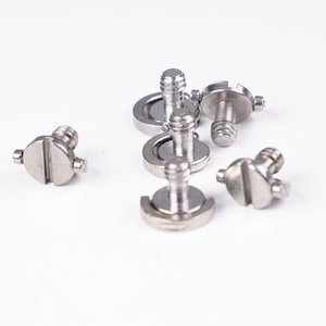 Puede incluir: Seis adaptadores de tornillo de trípode de cámara de metal plateado. Los tornillos tienen un eje roscado y una cabeza plana con una ranura para un destornillador.