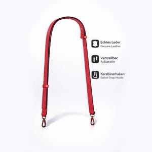 Könnte beinhalten: Ein roter Leder-Taschenriemen mit schwarzem Rand und verstellbarer Länge. Der Riemen verfügt über Karabinerhaken und ist als echtes Leder gekennzeichnet.