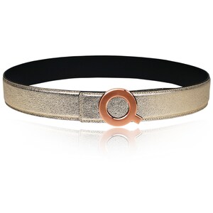 May include: A gold leather belt with a rose gold circular buckle featuring a stylized letter Q.