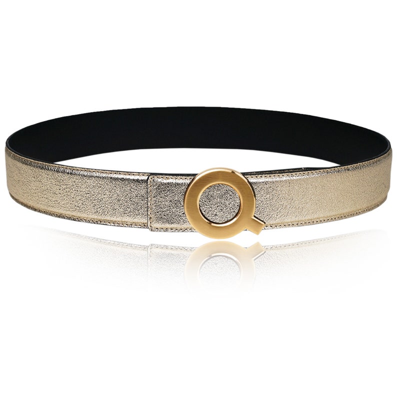 May include: A gold-colored leather belt with a large, gold-toned, circular buckle featuring a stylized letter "Q".