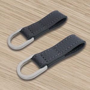 May include: Two dark grey leather loops with silver metal rings. The loops are stitched with a light grey thread.