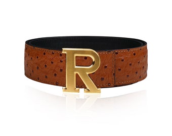 May include: A brown leather belt with an ostrich-embossed pattern and a gold-tone buckle featuring the letter "R".