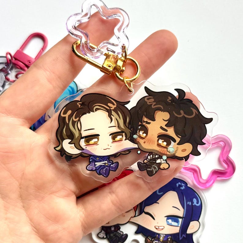 May include: Clear acrylic keyrings featuring cartoon characters with gold-coloured hardware. The keyrings have a star-shaped top and a gold clasp. The characters have detailed facial expressions and are wearing various outfits.
