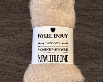 May include: A beige fuzzy blanket with a white tag that says "Rylee, Enjoy these cozy moments with your new little one".