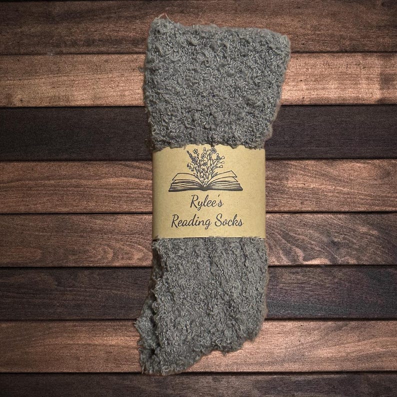 Pu&ograve; includere: Calzini grigi e pelosi con un'etichetta di carta marrone che dice "Rylee's Reading Socks" con un disegno di un libro e fiori.