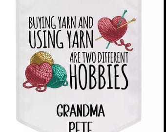 May include: White banner with the text "BUYING YARN AND USING YARN ARE TWO DIFFERENT HOBBIES." The banner features illustrations of yarn balls in red, gold, and teal, and a heart-shaped yarn ball with knitting needles. The name "GRANDMA PETE" is at the bottom.