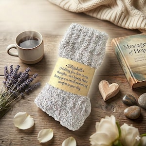 May include: A pair of fuzzy light gray socks wrapped in a tan paper band with the printed text: Elizabeth. Holding you close in my thoughts, and hoping these bring you a small moment of comfort to your day. The socks have a soft, textured knit.