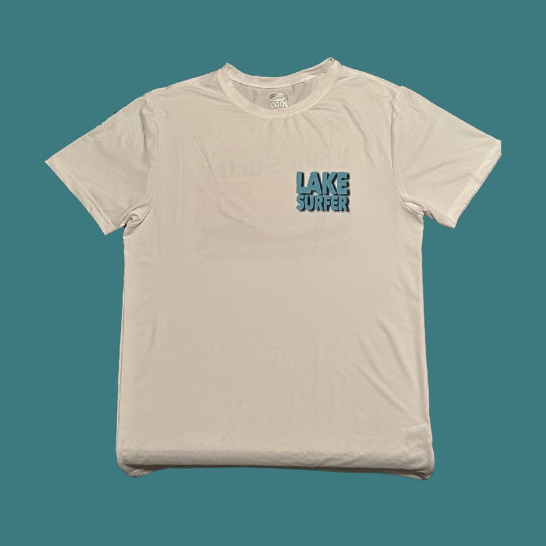May include: White t-shirt with a blue graphic that says "LAKE SURFER" on the front.
