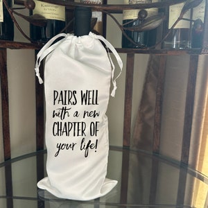 May include: White wine bottle bag with black text that reads "Pairs well with a new chapter of your life!"