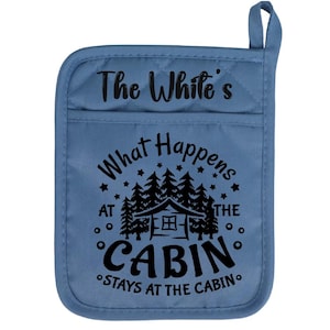 May include: A blue quilted oven mitt with the text "The White's What Happens at the Cabin Stays at the Cabin" in black. The design includes a cabin and trees.