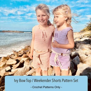 May include: Two young girls wearing matching crochet sets, one in pink and the other in lavender, stand on rocks near the ocean. The sets include a top and shorts. Text on the image reads: Ivy Bow Top / Weekender Shorts Pattern Set - Crochet Patterns Only -