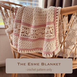 May include: A cream-coloured crocheted blanket with pink stripes and edging, draped over a wooden chair. The blanket features a detailed openwork design. Text on the image reads "The Esme Blanket - crochet pattern only -."