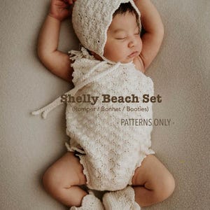 May include: A newborn baby wearing a cream-colored crochet romper, bonnet, and booties set. The set is labeled "Shelly Beach Set" and is a pattern. The baby is lying on a neutral-toned surface with arms raised.