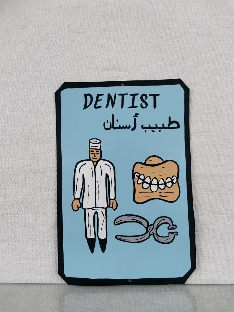 May include: A blue and black sign with the word "DENTIST" in white lettering. The sign also includes the Arabic text "طبيب أسنان" and a cartoon illustration of a dentist, a set of teeth, and a pair of pliers.