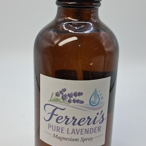 Puede incluir: Una botella de vidrio marrón con un pulverizador negro y una tapa transparente. La etiqueta dice "Ferreri's Pure Lavender Magnesium Spray" con una ramita de lavanda y un gráfico de gota de agua.