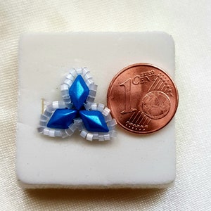May include: A small blue and white beaded flower design, approximately the size of a 1 Euro cent coin.