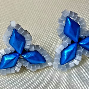 May include: A pair of blue and white beaded earrings in the shape of a three-leaf clover. The earrings are made with small, round beads and have a shiny, metallic finish.