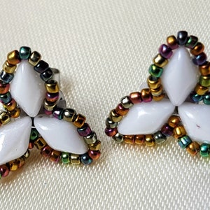 May include: A pair of white flower-shaped earrings with a multi-coloured beaded border. The beads are iridescent and include gold, green, red, and purple.