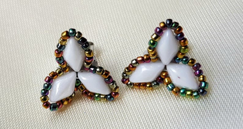 May include: A pair of white flower-shaped earrings with a multi-coloured beaded border. The beads are iridescent and include gold, green, red, and purple.