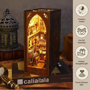 May include: A detailed, illuminated wooden bookshelf diorama. The miniature library scene features tiny books, furniture, and warm lighting. The diorama is designed to resemble a book and includes the text "caliaitalia".