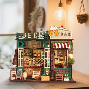 May include: A detailed miniature wooden bar model, featuring the word "BEER" and a sign saying "BAR". The model includes a red and white striped awning, a "VANCHY TAVERN" sign, and shelves filled with tiny bottles and glasses.