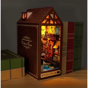 May include: A detailed, illuminated diorama of a town scene, housed within a book-shaped structure. The brown exterior features the text "Welcome to fairy tale town Colmar Town". The interior shows a street with balconies and flowers. Books are to the right.