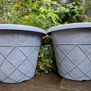 May include: Two grey plant pots with a diamond pattern and leaf design. The pots have a wide rim and are made of a durable material. Suitable for outdoor use, they add elegance to any garden or patio. Each pot is approximately 40 cm in diameter.