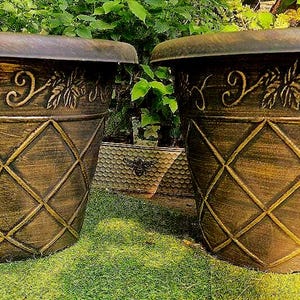 May include: Two matching tapered plant pots with a dark bronze finish. Each pot features a raised diamond lattice pattern on the lower section and a decorative band of embossed leaves and vines around the upper rim, creating a textured appearance.