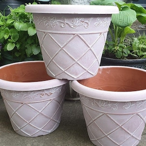 May include: Three decorative pink flower pots with a diamond pattern and a floral design. The pots are made of plastic and are ideal for indoor or outdoor use.