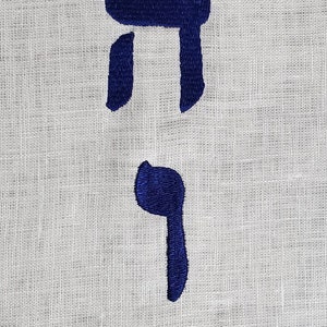 Op de afbeelding: Een witte stof met het Hebreeuwse woord "Chai" geborduurd in blauwe draad.