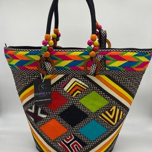 May include: A large, colorful tote bag with a black background and a geometric pattern. The bag has a zipper closure and two black handles with wooden beads. The bag has a label that says "Sophia's" and a website address.