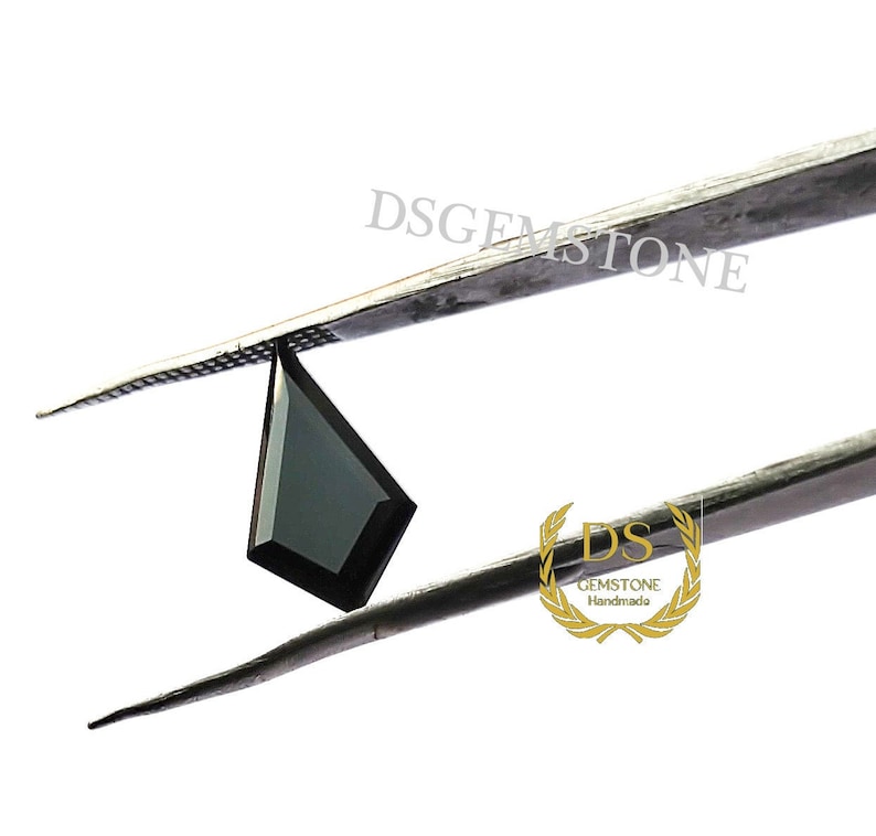 May include: A kite-shaped black gemstone held by metal tweezers. The stone features a faceted surface with sharp, geometric edges. The text DSGEMSTONE is visible above the stone, and a gold logo with the text DS GEMSTONE Handmade is below.