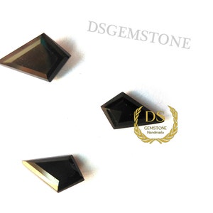 May include: Three black kite-shaped gemstones with faceted surfaces arranged on a white background. The text DSGEMSTONE appears in the upper right, and a gold laurel wreath logo with the text DS GEMSTONE Handmade is visible near the center.