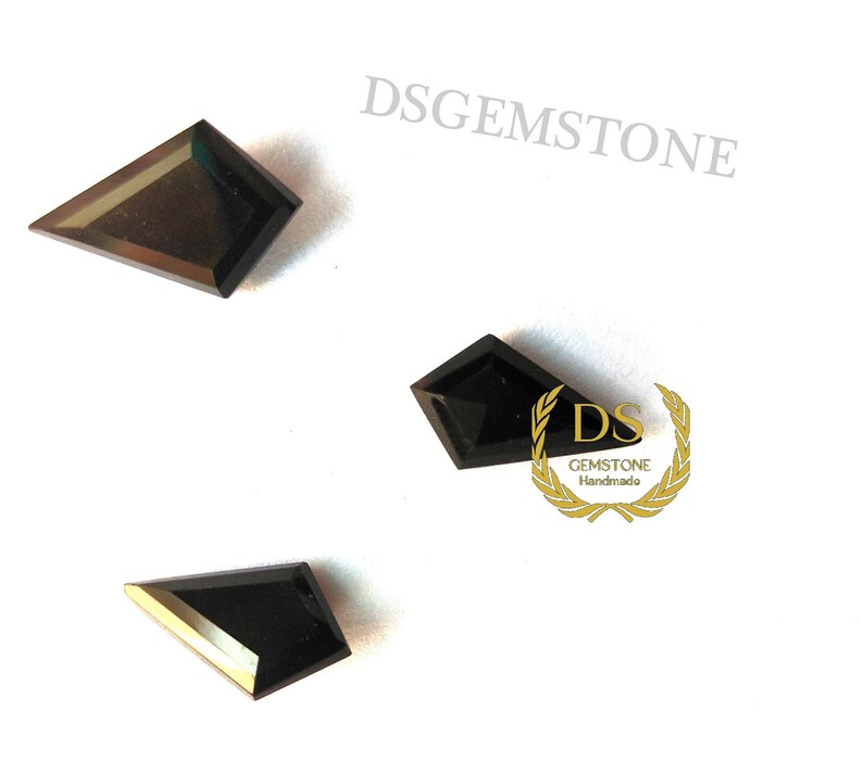 May include: Three black kite-shaped gemstones with faceted surfaces arranged on a white background. The text DSGEMSTONE appears in the upper right, and a gold laurel wreath logo with the text DS GEMSTONE Handmade is visible near the center.