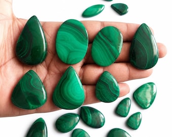 May include: A collection of polished malachite gemstones in various shapes, including teardrops, ovals, and irregular forms. The stones display a rich, deep green color with swirling patterns. The gemstones are displayed on a hand.